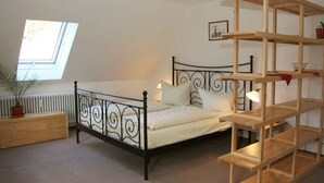 A bedroom with a bed, a window, a radiator, a wooden nightstand, and a wooden shelf unit. - Appartementhaus Am Roten Platz (Titisee-Neustadt)