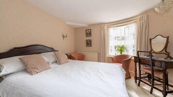 Habitació d'hotel amb un llit gran, un escriptori amb cadira, una finestra amb cortines i un penjoll.
