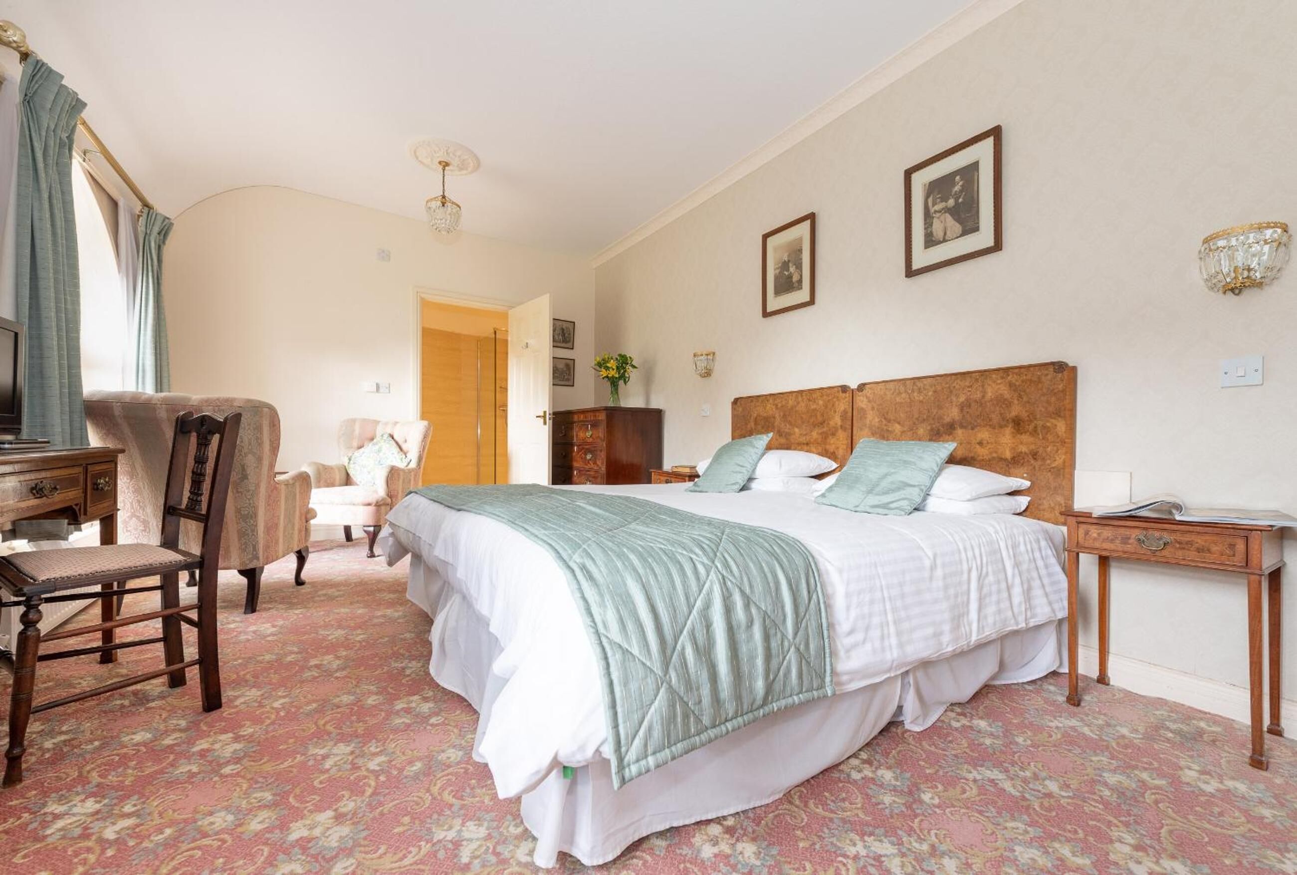 A hotel room with a large bed, a desk with a chair, a dresser, and a small table.