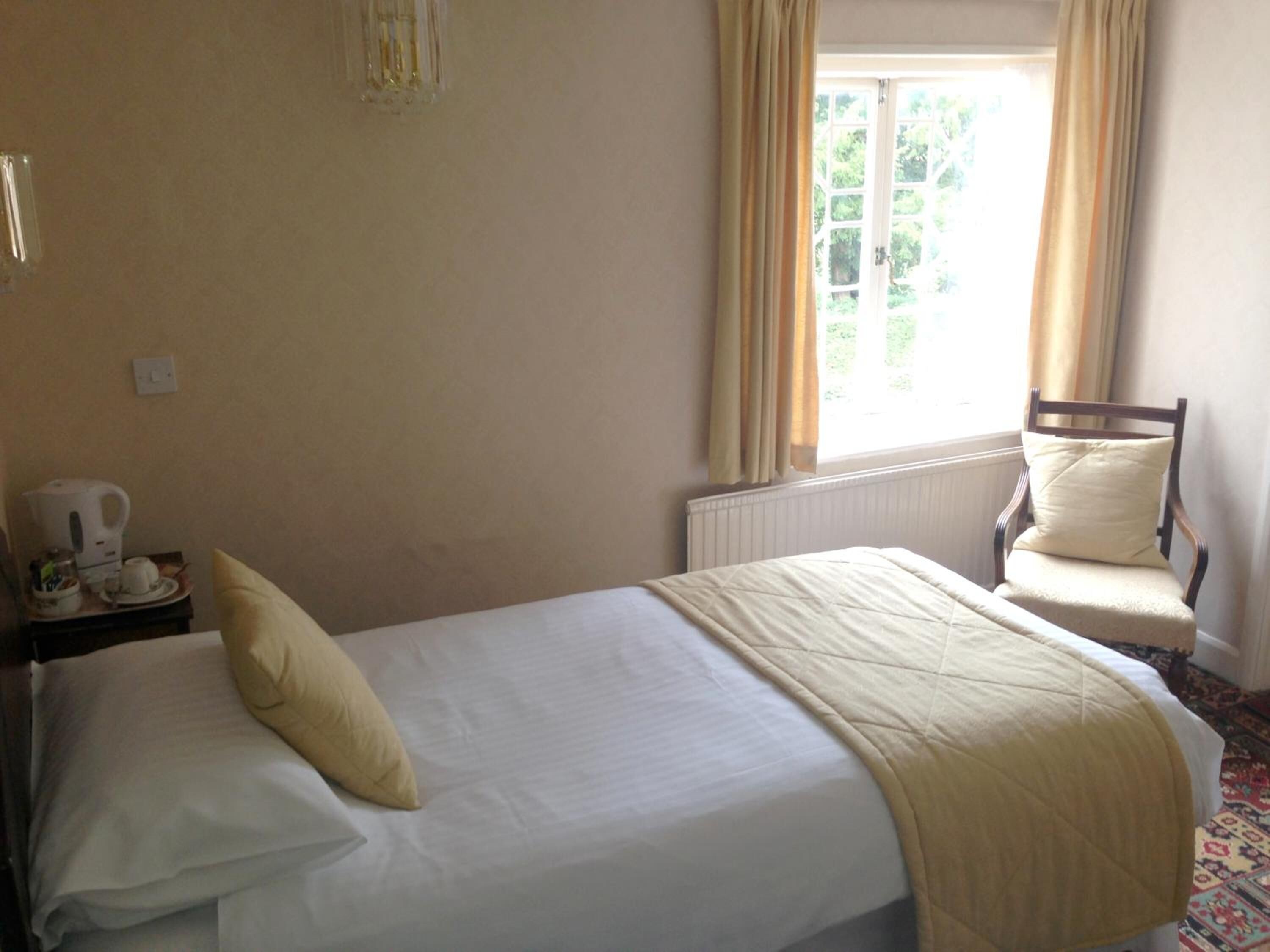 A hotel room with a bed, a chair, a radiator, and a window with curtains.