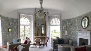 Una habitación amplia con chimenea, dos ventanas grandes con vidrieras y un candelabro.