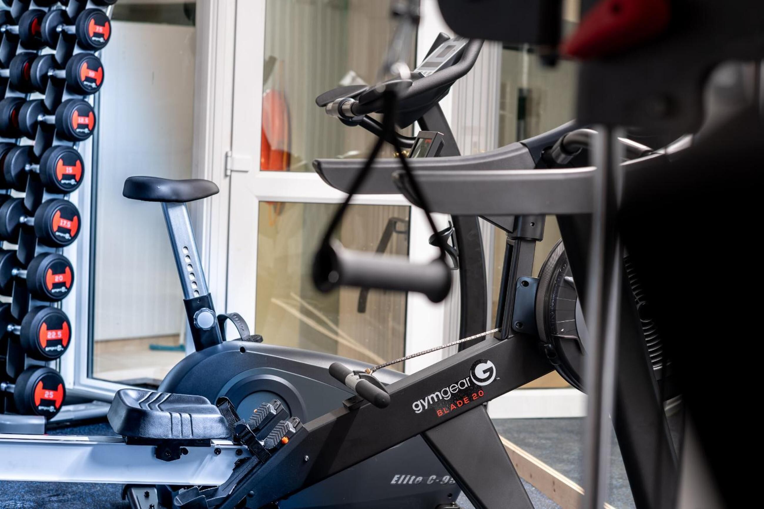 Un gimnasio con una bicicleta estática, un estante de mancuernas en la pared y un ventanal.