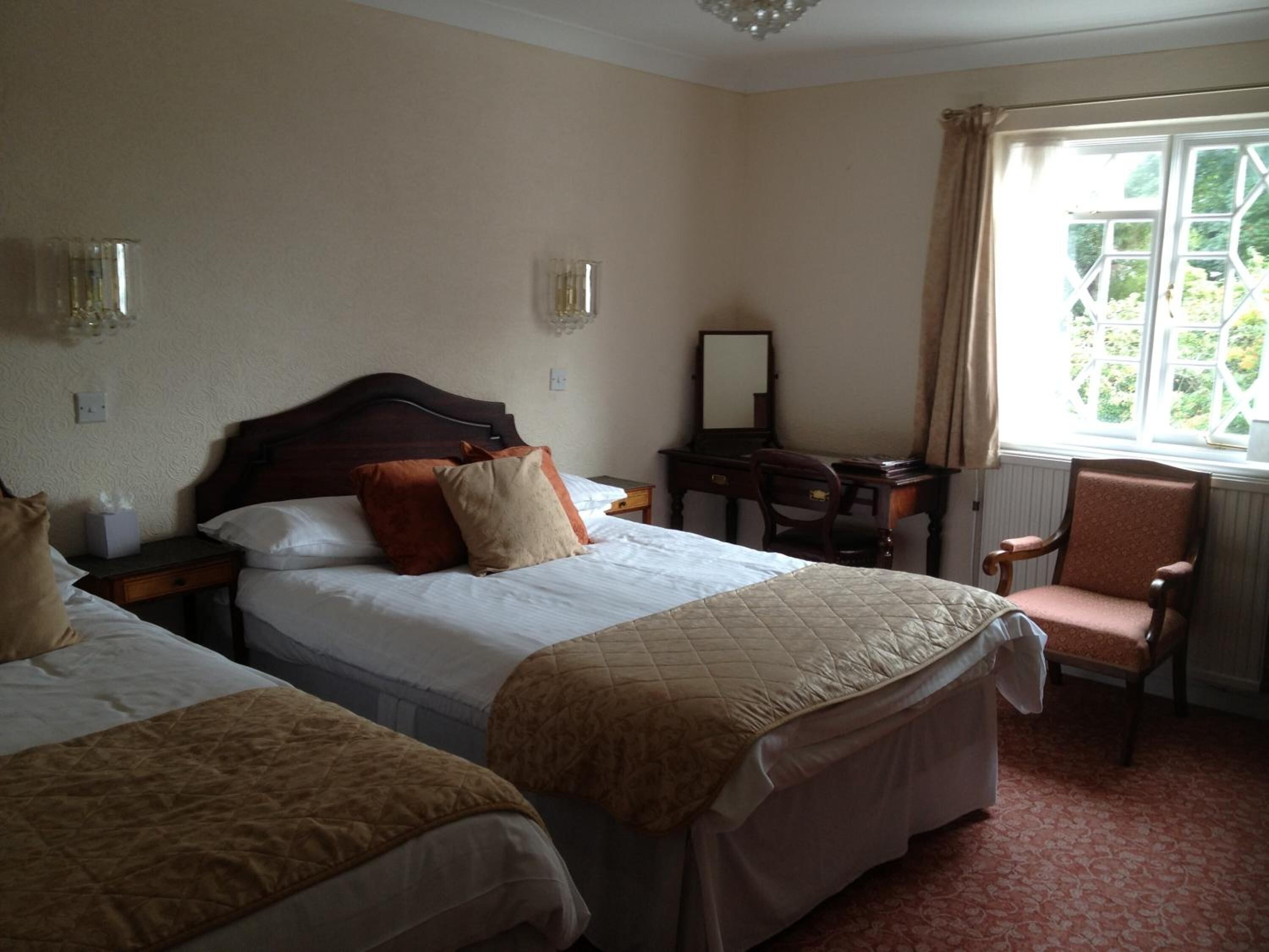 Habitación de hotel con dos camas, un escritorio, una silla y una ventana que ofrece vistas al verdor.