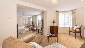 Una habitación amplia con una cama grande, una zona de estar con sofá y sillón, un aparador de madera y una mesa de comedor con sillas.