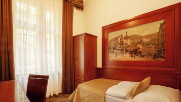 A hotel room with a bed, a wooden cabinet, a dining table with chairs, and a large framed picture on the wall.