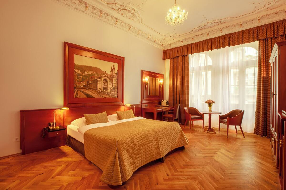 Habitación de hotel con una cama grande, un escritorio, una silla y una pequeña mesa con un jarrón.