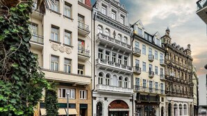 En rad historiska byggnader, med en central byggnad som har ett klocktorn, ett café och en hotellentrén.