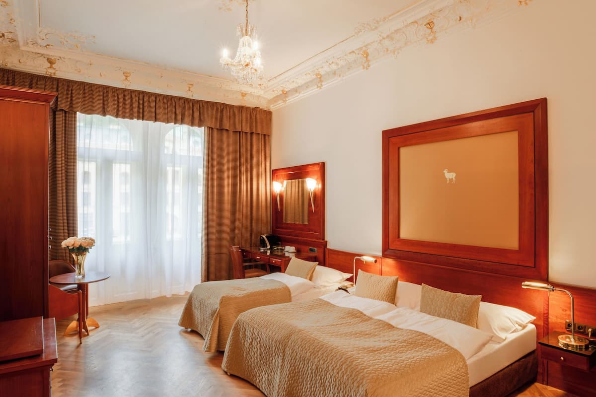Habitación de hotel con dos camas, un escritorio, una silla, tocador con espejo y una araña.