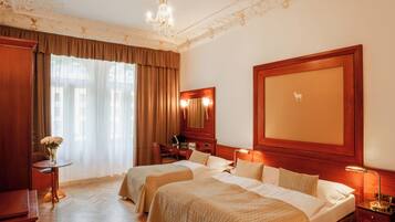 Ein Hotelzimmer mit zwei Betten, einem Schreibtisch, einem Sessel, einem Schminktisch mit Spiegel und einer Kristallleuchtre.