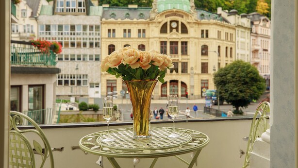 En balkong med ett bord, en vas med blommor och två glas champagne.