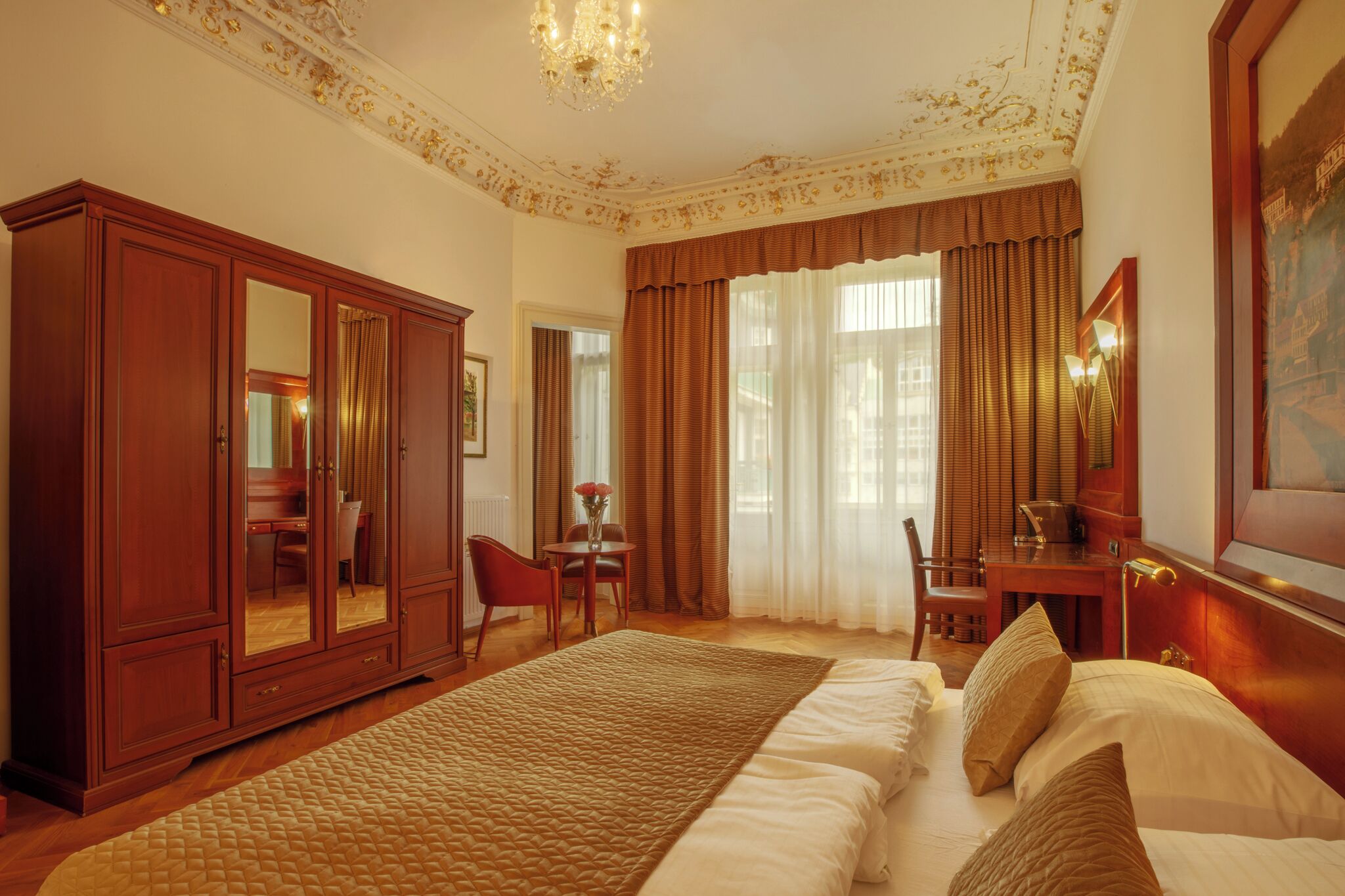 Ruime hotelkamer met een groot bed, een houten garderobe, een bureau met stoel en een grote spiegel.