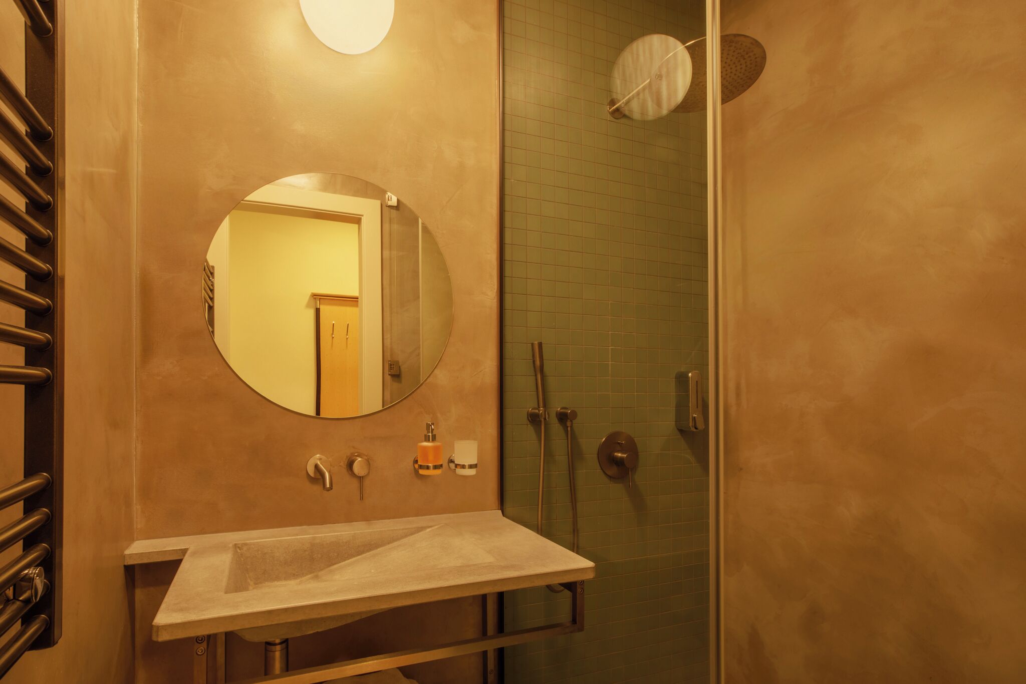 A bathroom with a round mirror, a sink, and a shower area.