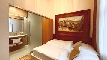 A hotel room with a bed, a painting, a bathroom with a mirror, and a wardrobe.