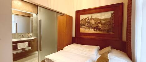 A hotel room with a bed, a painting, a bathroom with a mirror, and a wardrobe.
