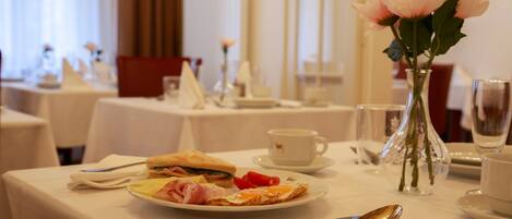 A dining table with a sandwich, a plate with a slice of toast, a cup, and a vase with flowers.