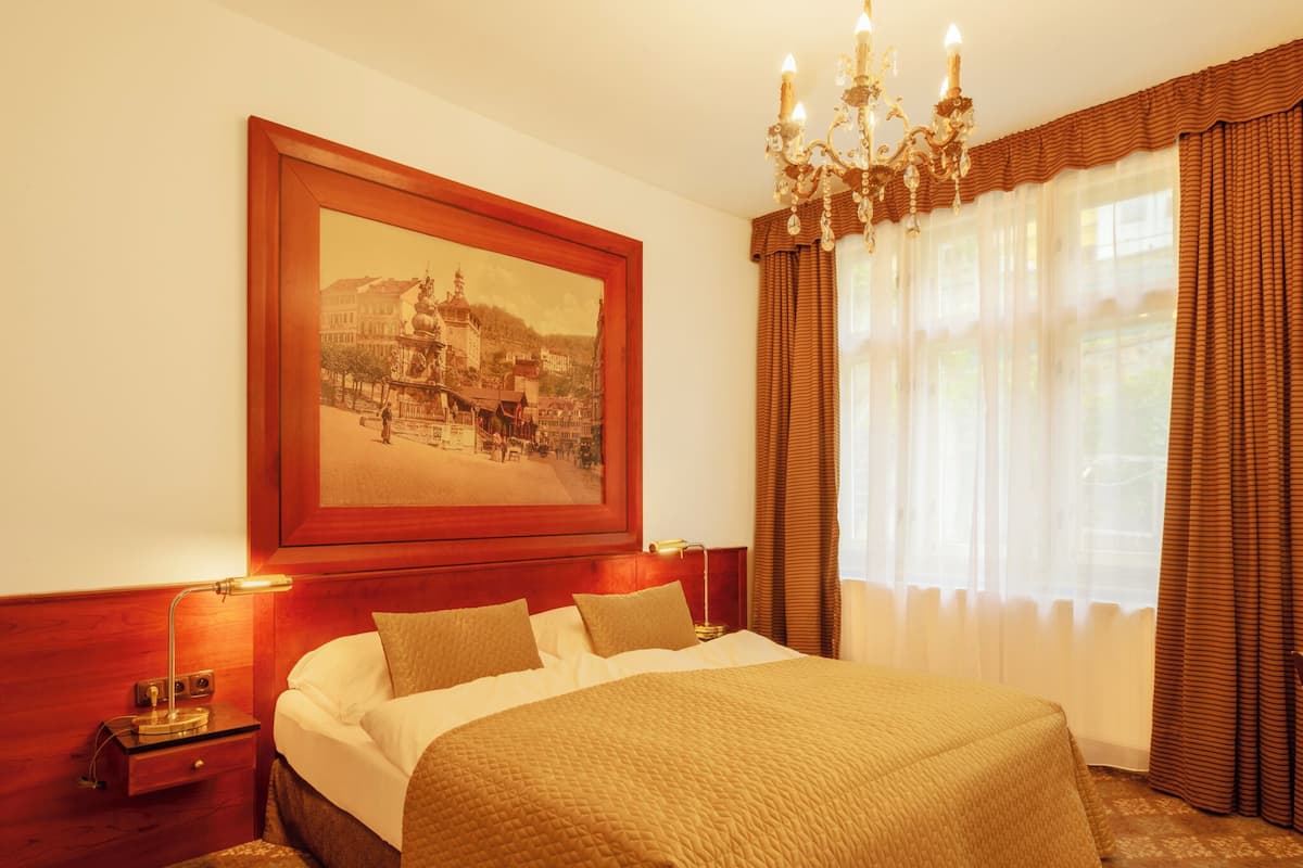 Habitación de hotel con una cama grande, una mesita de noche, una lámpara, un candelabro y un cuadro grande enmarcado en la pared.