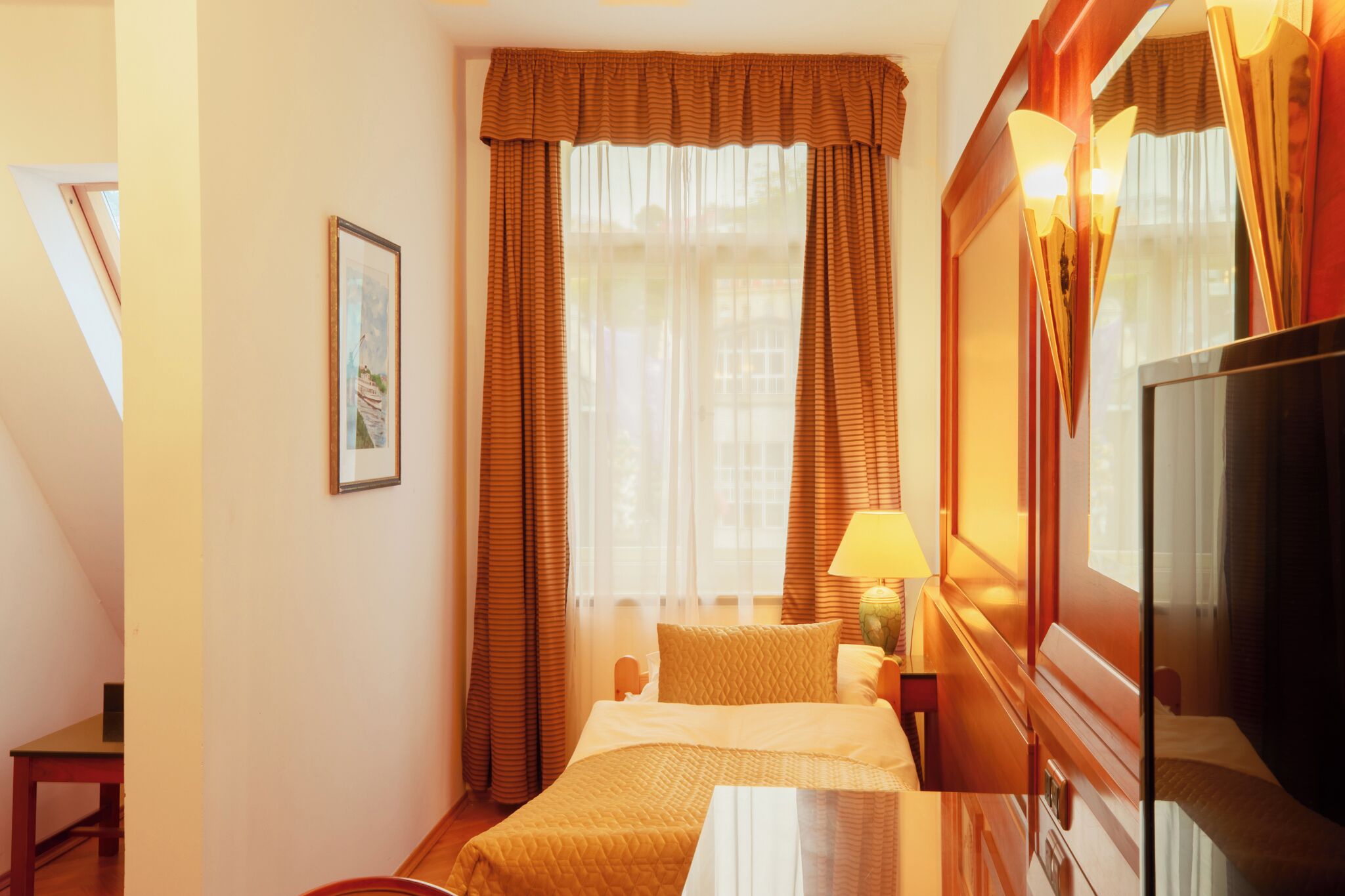 A hotel room with a bed, a bedside table, a lamp, and a television.