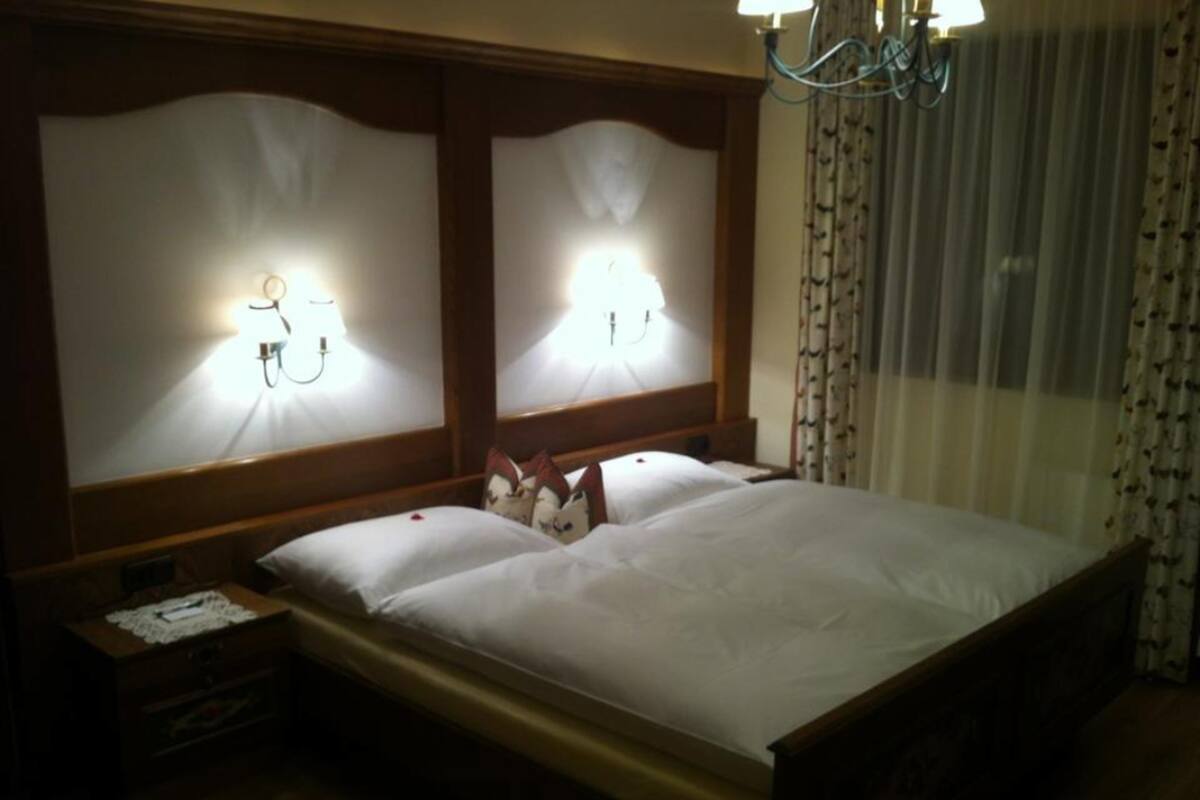 A hotel room with a wooden bed, two bedside lamps, a nightstand, and a chandelier.
