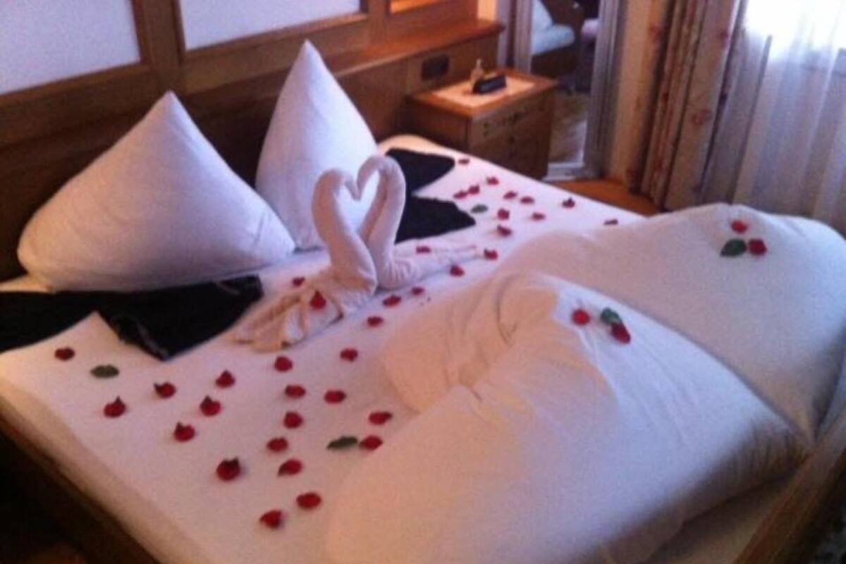 A hotel room with a neatly made bed, pillows, and a heart-shaped towel arrangement.