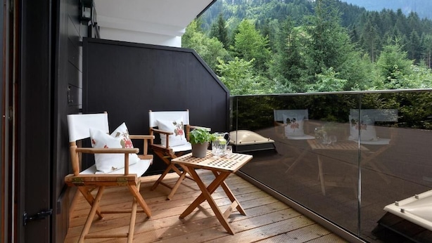 Ein Balkon mit Holzstühlen und einem Tisch, mit Blick auf eine bewaldete Berglandschaft.