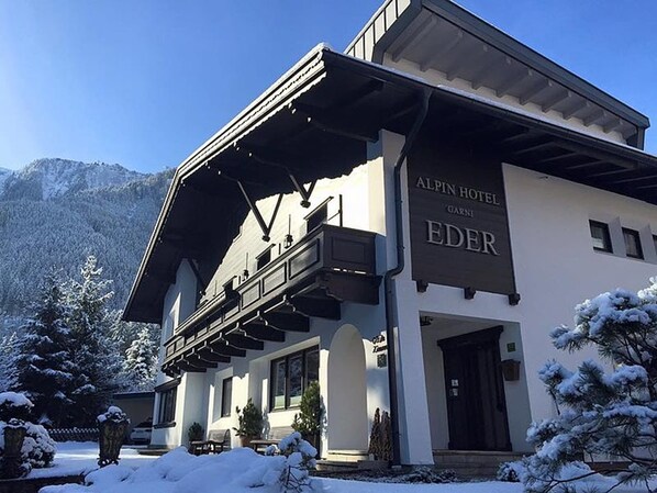 A hotel with a modern architectural style, featuring a prominent balcony and a sign that reads "ALPIN HOTEL EDER."