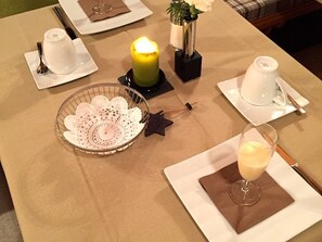 A table set for a meal with white dishes, a candle, and a glass of a light-colored beverage.