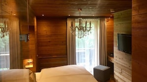Ein Zimmer in einer Holzhütte mit einem Bett, einer Chandelüster, einem Fernseher und einem Fenster mit Vorhängen.
