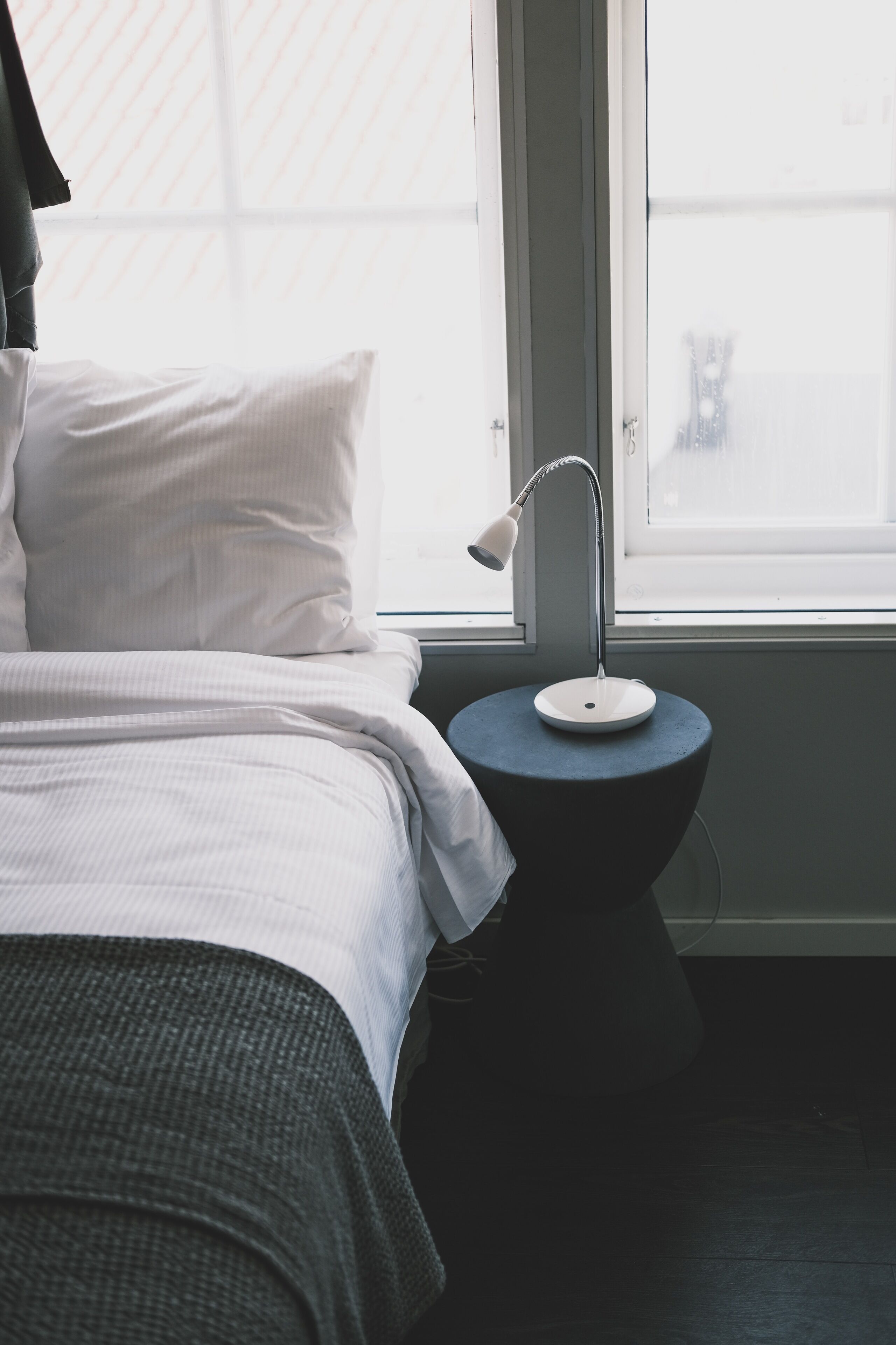 Un dormitorio con una cama, una mesita de noche con lámpara y una ventana.
