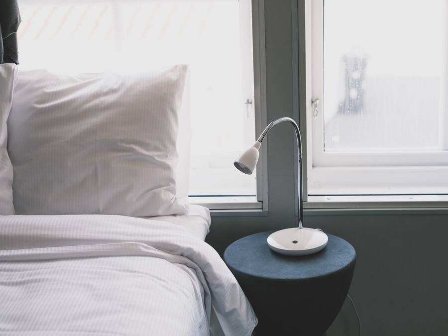 Un dormitorio con una cama, una mesita de noche con lámpara y una ventana.