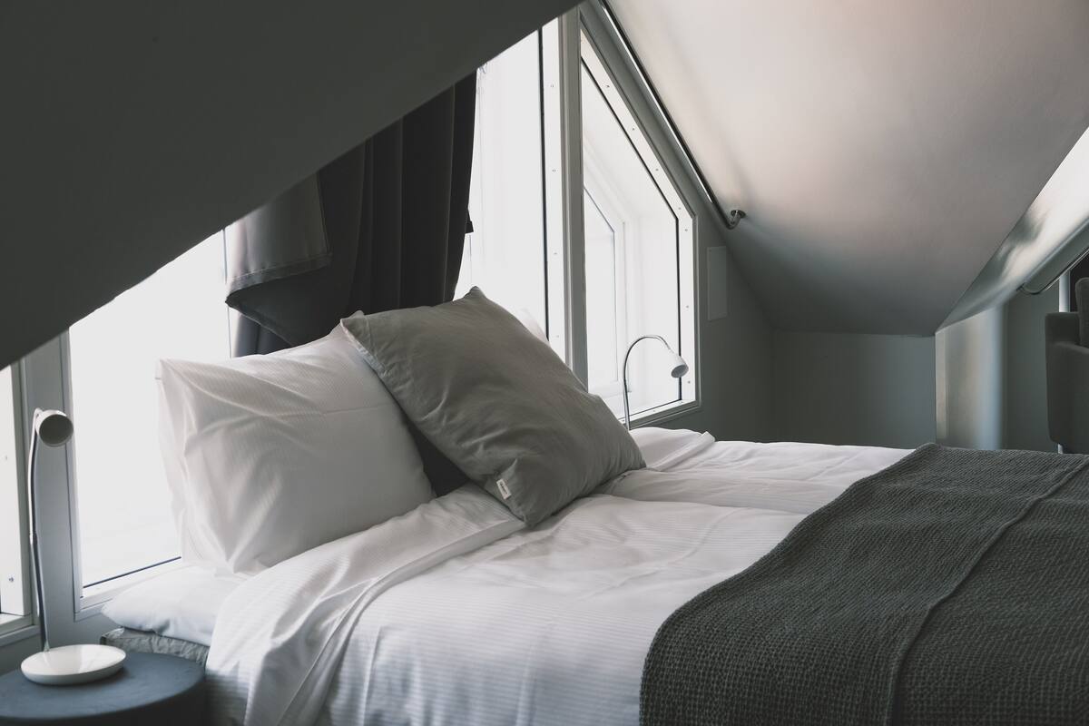 A bedroom with a bed, pillows, a bedside table, and a window.