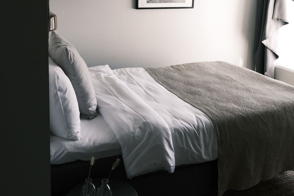 A bedroom with a bed, a small round table, a framed picture on the wall, and a window with curtains.