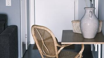 Una habitación con una silla de mimbre, una mesita, un jarrón y un sofá gris.