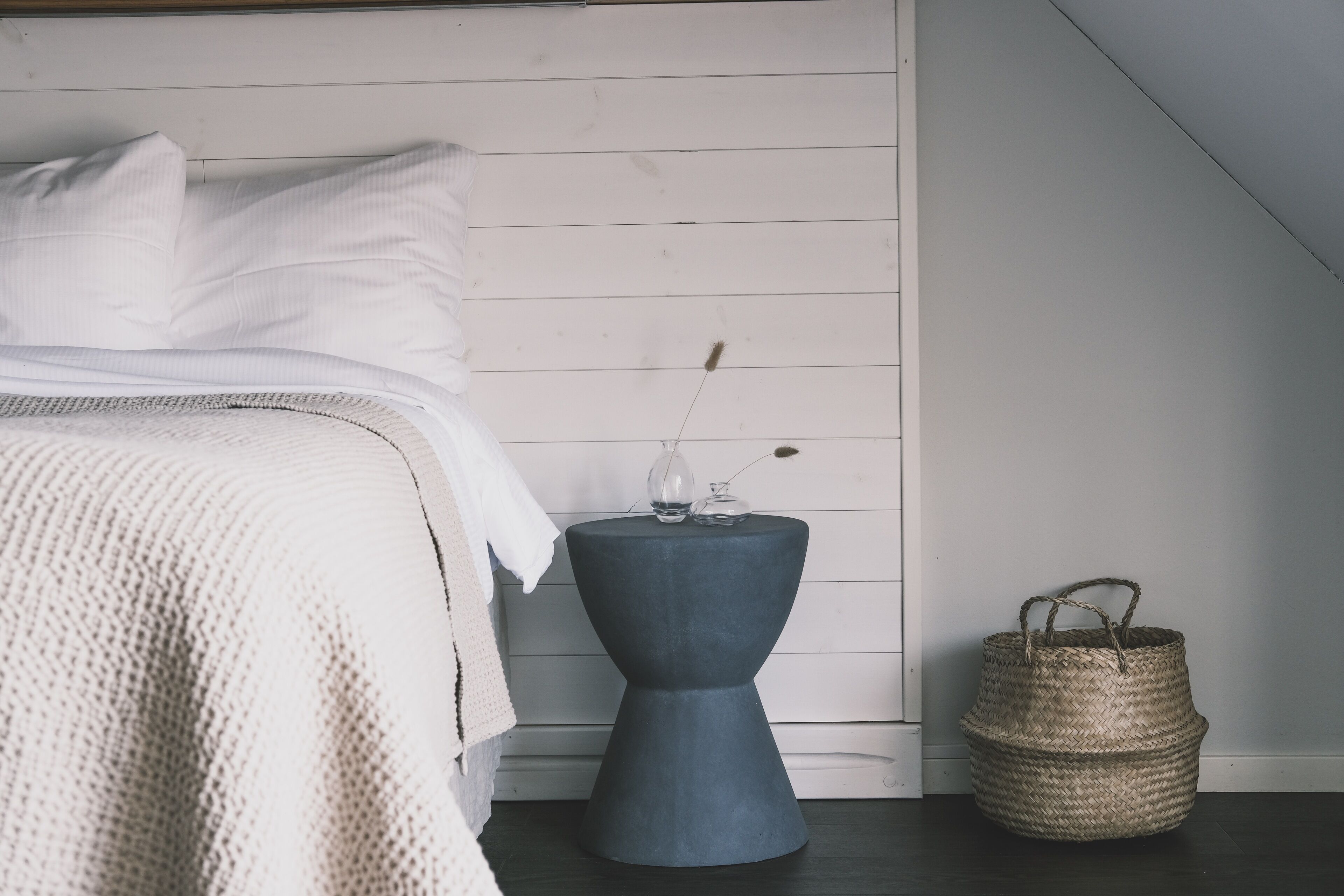 A bedroom with a bed, a bedside table with a vase, and a woven basket.