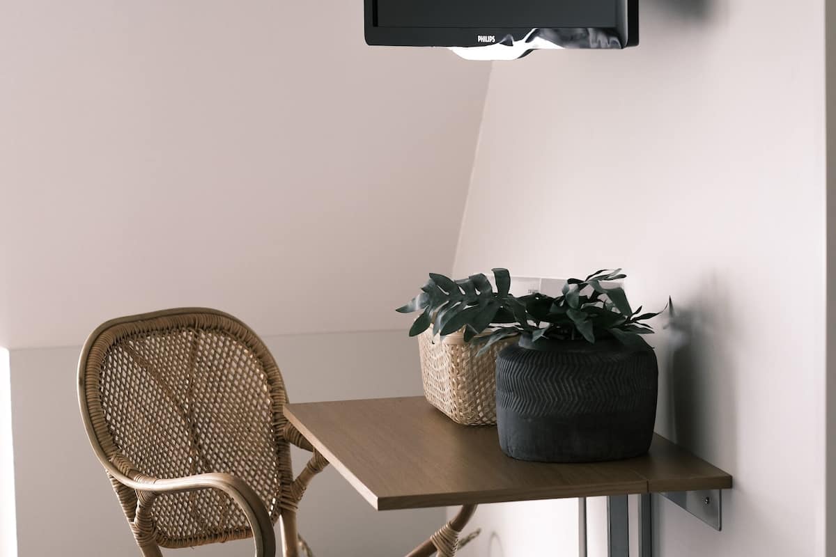 A room with a mounted TV, a wicker chair, a small table with a plant, and a dark wooden floor.