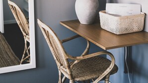 A room with a wooden table, wicker chairs, a white vase with dried plants, a flat-screen TV, and a mirror on the wall. - Skärgårdshotellet Hönö (Hono)