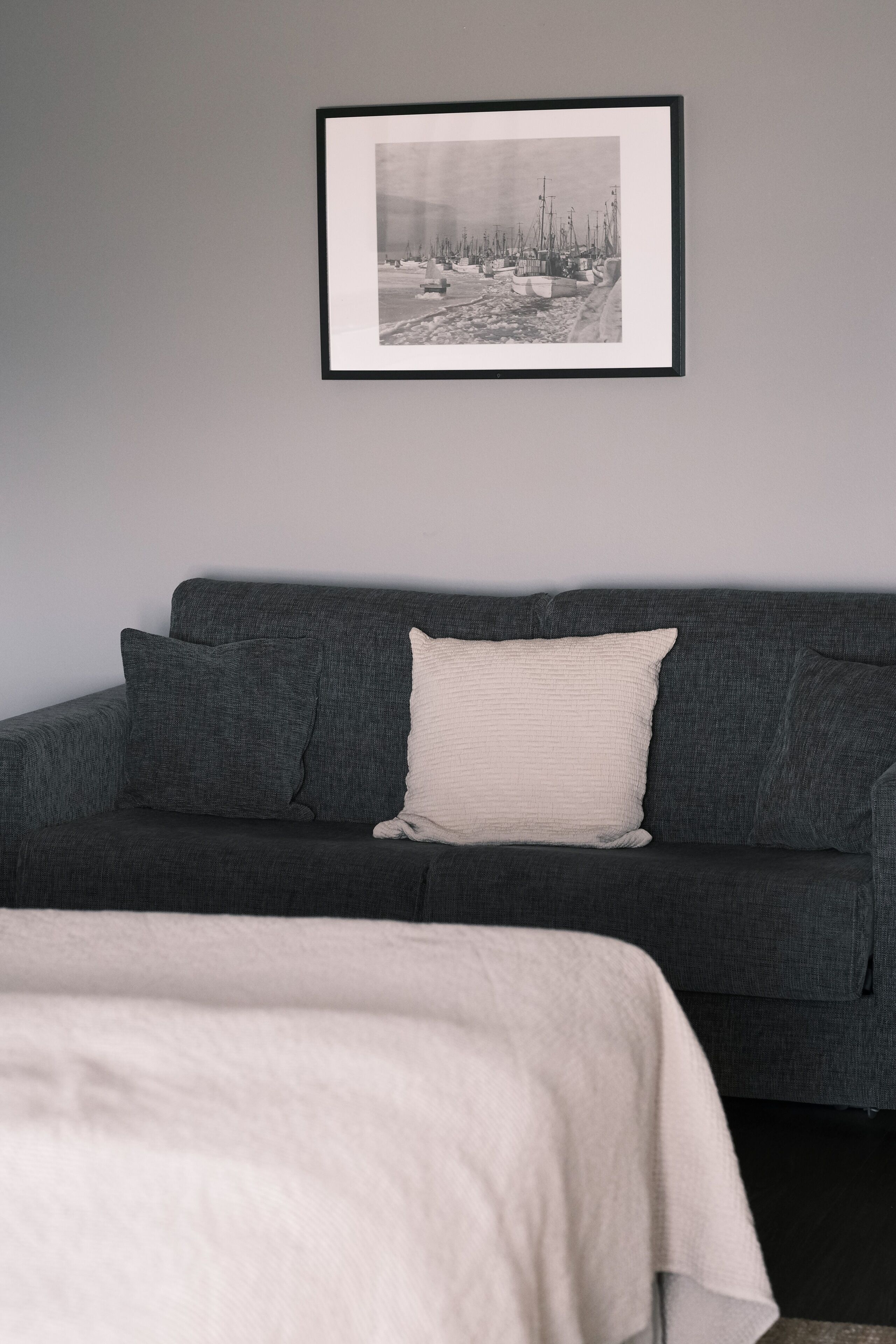 Una habitación moderna con un sofá gris oscuro, una almohada blanca y una fotografía blanco y negro enmarcada en la pared.