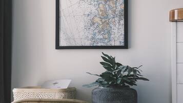 A room with a wicker chair, a framed map on the wall, and a potted plant on a shelf.