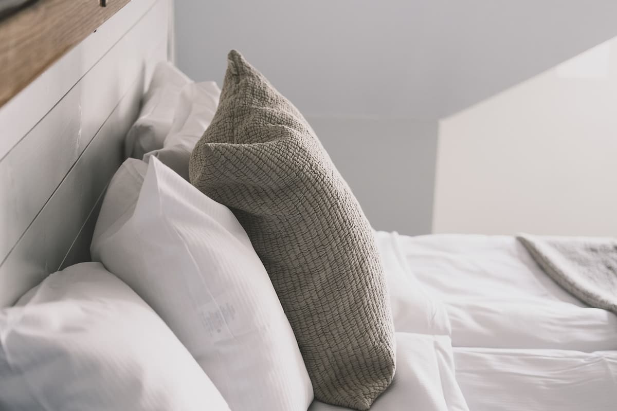 A neatly made bed with white linens and a wooden headboard.