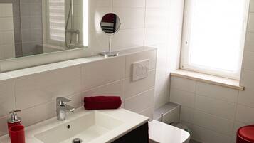 Un baño moderno con un lavabo blanco, un mueble negro, una toalla roja y una ventana con persianas.