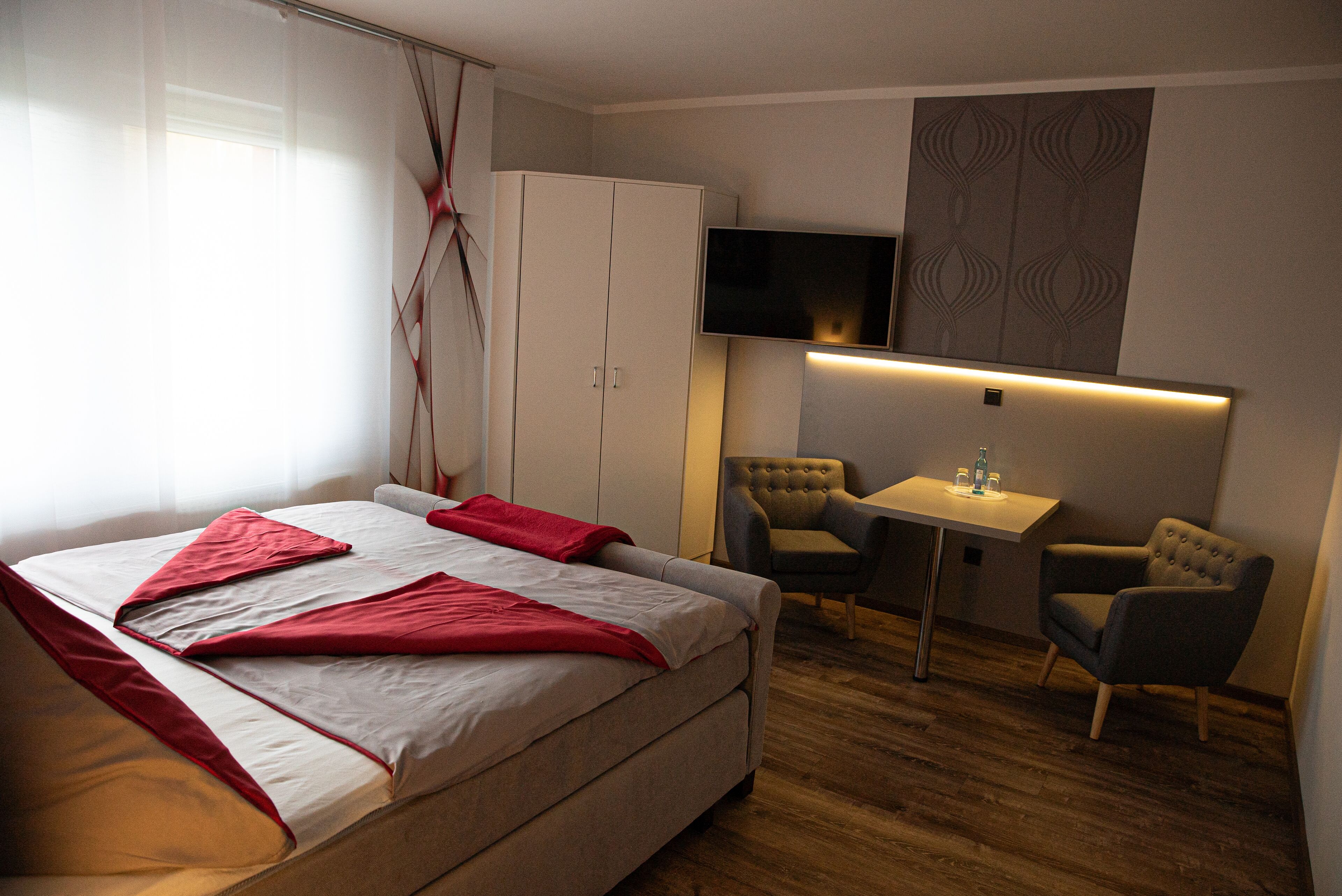 A hotel room with a bed, a desk, two chairs, a TV, and a wardrobe.