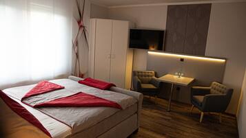 A hotel room with a bed, a desk, two chairs, a TV, and a wardrobe.