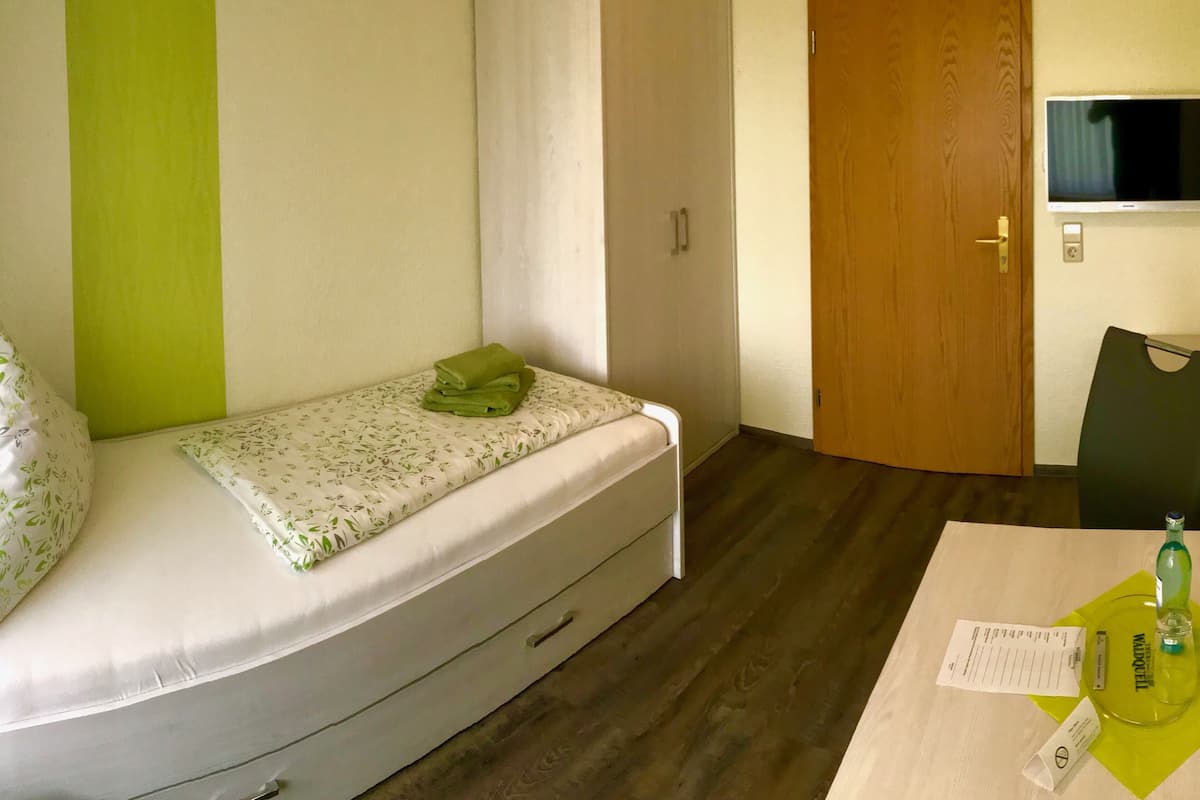A small bedroom with a bed, a wardrobe, a desk with a chair, and a television.