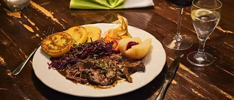 Un plato de comida con un cuchillo y un tenedor, una copa de vino tinto y una vela sobre una mesa de madera.