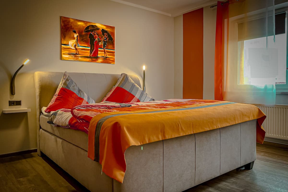 A bedroom with a bed, a painting on the wall, and a window with curtains.