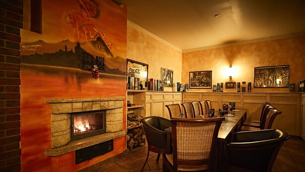 A cozy dining area with a fireplace, wooden chairs, and a long table. - Restaurant & Pension Rüssel - Pub (Sangerhausen)