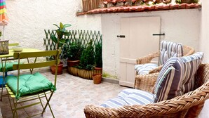 A patio with a wicker sofa, a green folding chair, and a table with a bowl. There are potted plants and a wooden fence. - B&B Il Tomolo (Agnone)