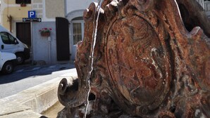A rustic fountain with water flowing, set against a building with a balcony and a car parked nearby. - B&B Il Tomolo (Agnone)