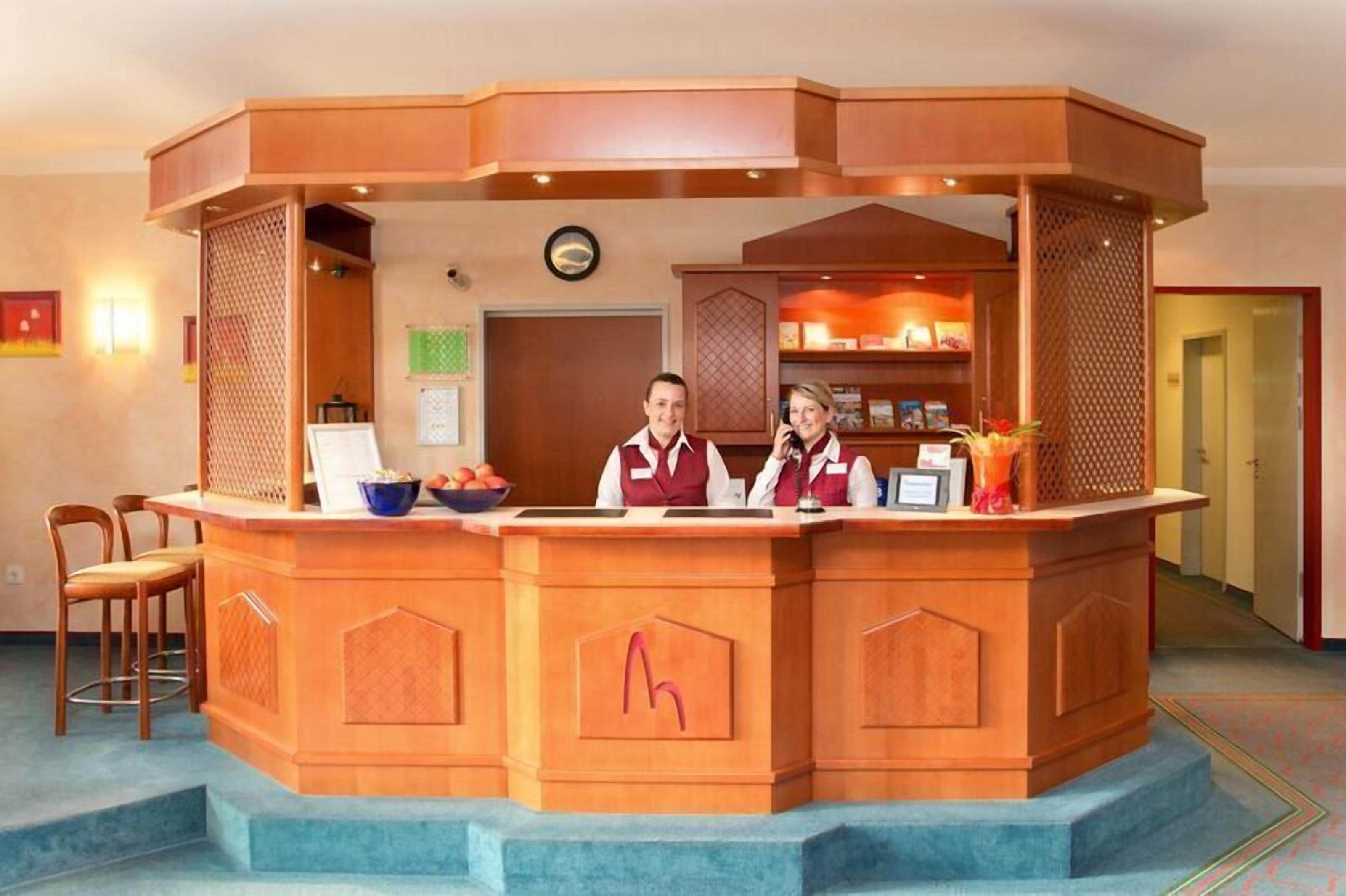 A reception desk with two staff members, a clock, and a small seating area with chairs.