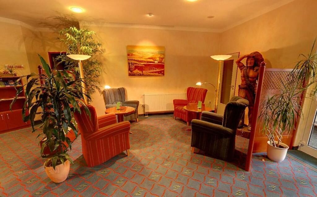 A hotel lobby with a patterned carpet, several armchairs, a sofa, and potted plants.