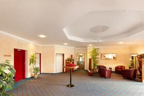 Eine Hotellobby mit einem gemusterten Teppich, roten Türen und mehreren Blumentöpfen.